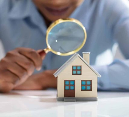 Businesswoman Holding Magnifying Glass Over House Model